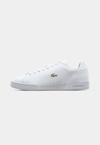 Biele tenisky Lacoste, hladký syntetický materiál, okrúly špička, šnurovanie na sedem dierok, zlatý logový akcent na boku, textúrovaná gumová podrážka, plochý podpätok.