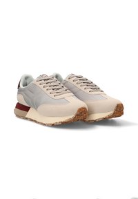 Zapatillas deportivas beige con acentos grises, tela texturizada, diseño de cordones y suela de goma marrón moteada. Presentan un ligero acolchado y soporte.