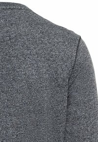 Grå, tekstureret stof af en sweater, der viser et tæt på billede af skuldersømmen og det bløde, strikkede materiale.