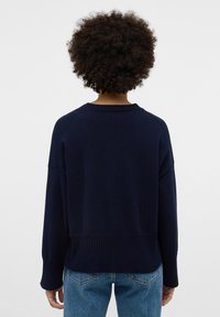 Marineblauer Strickpullover mit Rundhalsausschnitt, überschnittenen Schultern und geripptem Saum. Kombiniert mit hellblauen Jeans.