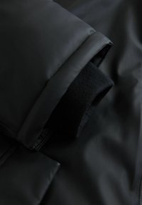 Juoda paminkšta striukė su lygiu išore ir matomi jaukūs juodi megzti rankogaliai. Turi elegantišką, vientisą konstrukciją matinio paviršiaus.