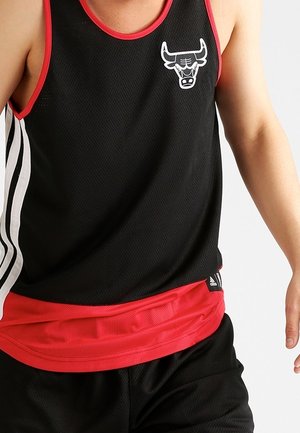 Personne portant un maillot de basket sans manches noir et rouge avec un logo des Chicago Bulls et un short noir.