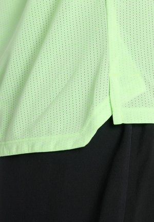 Tissu perforé vert clair superposé à un tissu noir, montrant la texture et les bords superposés des vêtements.