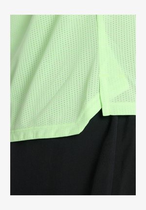 Tissu perforé vert clair superposé à un tissu noir, montrant la texture et les bords superposés des vêtements.