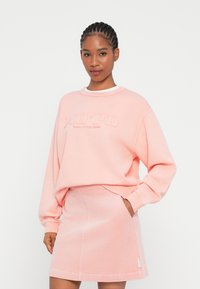 Sweatshirt rosa claro com gola redonda e logótipo bordado, combinado com uma saia de cotele correspondente com bolsos laterais e bainha sem costura.
