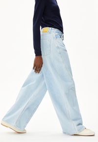 Lichtblauwe wijde jeans met een hoge taille, voorzien van een gele merklabel aan de achterkant en subtiele stikdetails. Zachte denimtextuur.