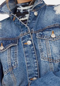 Spijkerjack in lichtblauw met een verweerde afwerking, zilverkleurige hardware, drukknopen en twee borstzakken met gestikte accenten.