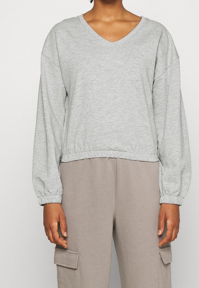 Pullover grigio a maniche lunghe con scollo a V e orlo arricciato. Tessuto morbido e texturizzato. Abbinato a pantaloni cargo beige con tasche laterali.