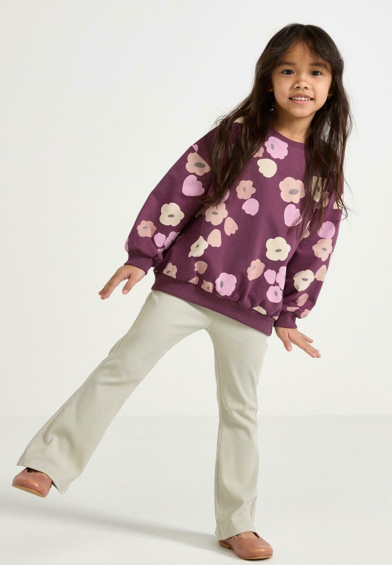 Lilla blomster sweatshirt med lange ærmer og ribbede manchetter, parret med lysebeige ribbede flared bukser. Brune sko fuldender outfittet.