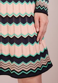 Stickad klänning med ett zigzag-mönster i pastellrosa, mintgrön och marinblå. Texturerad tyg med synlig sömnad och sprickor mellan färgerna.