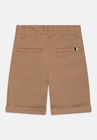 Pantaloni corti in cotone marrone con una texture liscia, dotati di doppie tasche posteriori e orlo arrotolato. Design semplice con sottili dettagli di cucitura.