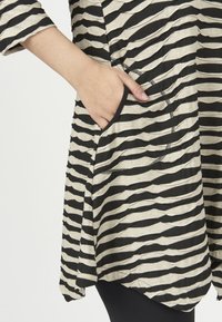 Stribet tunika i sort og beige, med en rund halsudskæring, lange ærmer og sidelommer. Blødt stof med et tekstureret, draperet design.