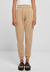 Beige joggebukser laget av mykt stoff, med elastisk midje med snøring, ribbestrikkede mansjetter og avslappet passform.