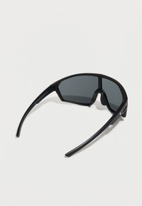 Μαύρα γυαλιά ηλίου με γεωμετρικό σχέδιο, σκοτεινούς φακούς και κομψό πλαστικό πλαίσιο. Διαθέτουν ομαλή υφή και ελαφρώς καμπυλωτούς βραχίονες.