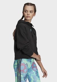 Svart kort hoodie med dragsnaror, prydd med en liten blå logotyp. Matchad med färgglada tryckta leggings med blommönster och svarta ränder.