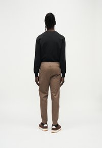 Chemise noire à manches longues en tissu texturé, associée à un pantalon marron fuselé avec poches et taille élastique. Baskets marron.