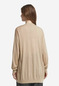 Beige leichter Pullover mit langen Ärmeln, runder Ausschnitt und gerafften Bündchen. Glatte Textur und lockere Passform.