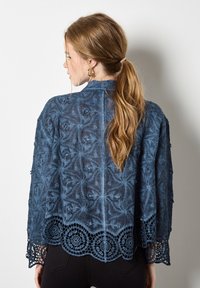 Cárdigan de ganchillo azul con intrincados patrones florales, tejido texturizado y dobladillo de encaje con forma de concha, con mangas tres cuartos y abertura delantera.