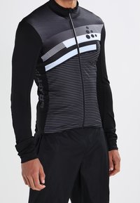 Černý cyklistický dres dlouhý rukáv s předním zipem, se vodorovnými pruhy a geometrickými vzory v bílé a šedé barvě.