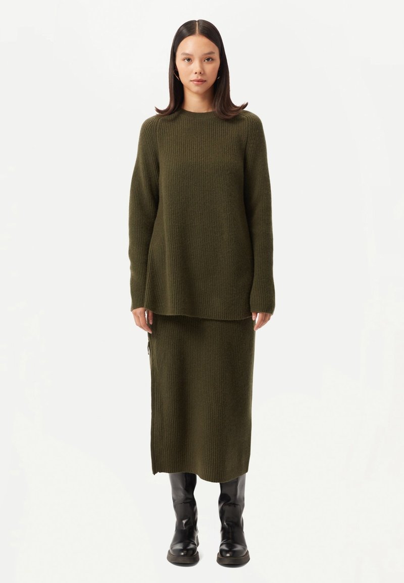 Pull à côtes vert olive et jupe assortie, en tissu tricoté texturé, associés à des bottes noires montantes. Design simple à coupe droite.