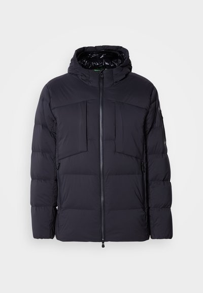 Veste noire rembourrée avec capuche, dotée d'une fermeture éclair sur le devant, de deux grandes poches poitrine et de poches latérales. Texture lisse et design matelassé.