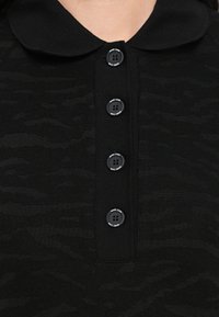 Polo noir avec un motif texturé, grand col et patte de boutonnage à cinq boutons noirs avec accents de logo.