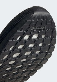 Semelle de chaussure de sport noire avec un motif de semelle présentant des découpes hexagonales et ovales ; caoutchouc texturé avec la marque "Continental".