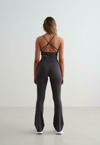 Crop top de sport noir avec des bretelles croisées et leggings noirs à taille haute évasés, tous deux fabriqués dans un tissu extensible et lisse.