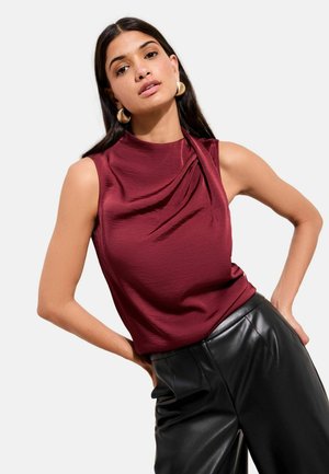 Burgundy sleeveless top with draped detailing at the shoulder, paired with black leather trousers, featuring a smooth texture and fitted design.