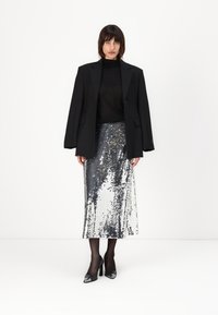 Zwarte oversized blazer over een zwart top, gecombineerd met een midi-jurk van zilveren pailletten. Zwarte sheer panty’s en zwarte puntige hakken maken de look af.