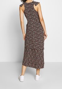 Vestido negro con estampado floral y mangas con volantes, que presenta un dobladillo a la altura de la rodilla y un diseño en capas, combinado con zapatillas blancas.