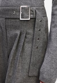 Grau Wollhosen mit einem breiten Gürtel, der über eine rechteckige Metallschnalle verfügt. Der Bund hat ein gefälteltes Design und dekorative Metalldruckknöpfe.