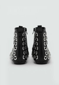 Botas negras hasta el tobillo de cuero, con grandes ojales plateados a los lados, textura suave y cierre con cremallera en la parte trasera.