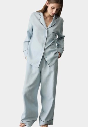 Hellblaues Pyjama-Set aus weichem Stoff, bestehend aus einem Hemd mit Knopfleiste und Brusttasche mit kontrastierender schwarzer Paspelierung, kombiniert mit locker sitzenden Hosen.