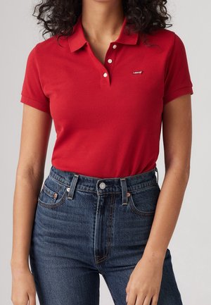 Punainen poolopaita, jossa on klassinen kaulus ja kolme nappia, sekä pieni Levi's-logo. Yhdistetty korkeavyötäröisiin, tummiin farkkuihin.