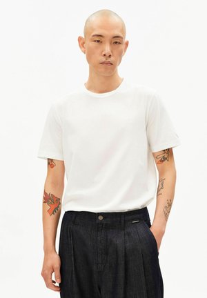 Weißes Baumwoll-T-Shirt mit Rundhalsausschnitt und kurzen Ärmeln, kombiniert mit dunkelblauen Jeanshosen mit Knopf und seitlichen Taschen.