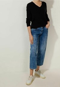 Black v-neck sweater, relaxed fit, with long sleeves; blue denim wide-leg jeans. White sneakers with textured accents complete the outfit.