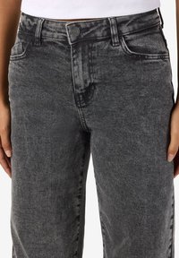 Högmidjade, raka jeans i svart denim med en blekt tvätt. Har klassiska fickor och knappar. Texturen verkar mjuk och något använd.