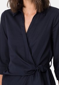 Vestido envolvente azul marino de tela suave, con cuello tipo polo, mangas de tres cuartos y detalle de cintura anudada.