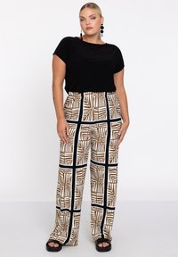 Schwarzes Kurzarmoberteil kombiniert mit lockeren, gemusterten Hosen, die braune und weiße Blattmuster in einem Rasterdesign aufweisen, mit einem schwarzen Bund.