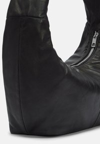 Borsa in pelle nera con una forma curva e zip argentata visibile su uno sfondo bianco semplice.