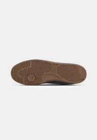Shoe sole with a honeycomb texture in brown rubber, featuring textured patterns and an embossed logo, set against a plain background.