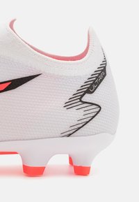 Scarpa da calcio bianca con tomaia testurizzata, caratterizzata da dettagli neri e rosa. Il tallone presenta il marchio "ULTRA" e tacchetti rossi per una migliore aderenza.
