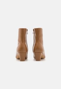 Bottes basses en cuir marron avec un bout pointu, un talon bloc de hauteur moyenne et une fermeture éclair latérale. Texture lisse avec peu de détails.