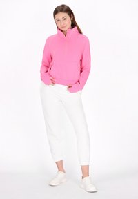 Rosa halvdraget tröja med känguruficka, som kombineras med vita byxor med elastisk vrist och ljusa sneakers. Slät textur och avslappnad passform.
