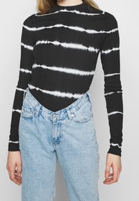 Sort langærmet top med hvide tie-dye striber, kombineret med lyseblå højtaljede jeans. Stoffet ser glat og tætsiddende ud.