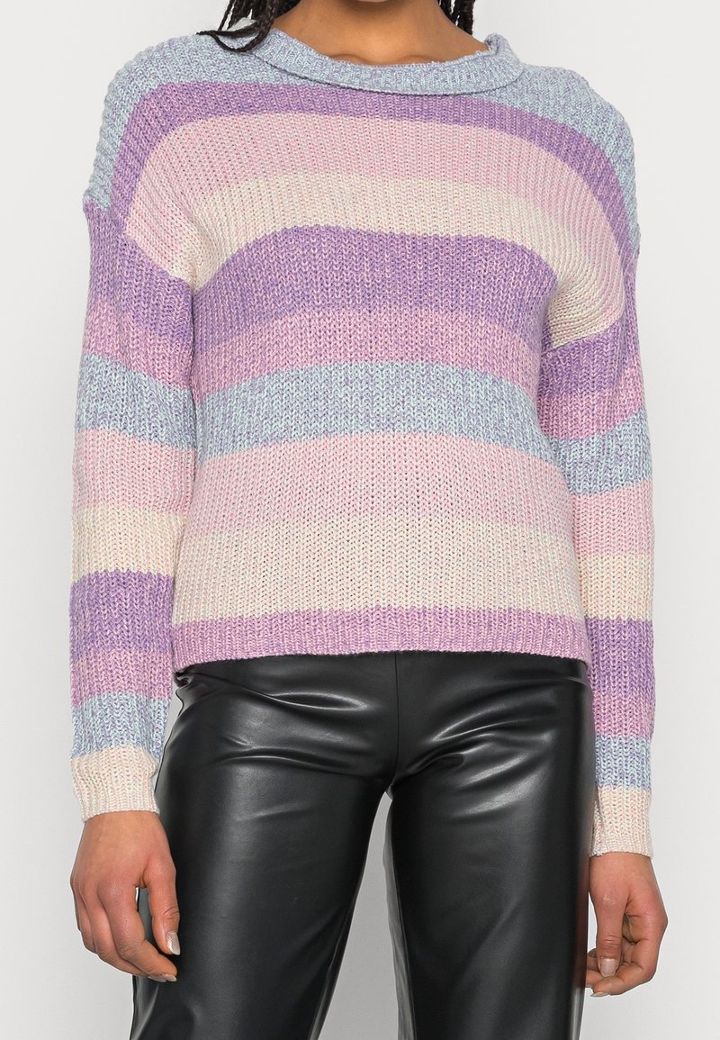 Pull en tricot à larges rayures horizontales lavande, rose, crème et bleu clair, porté avec un pantalon en cuir noir.