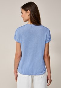 T-shirt bleu clair à manches courtes avec des poignets roulés, col rond et coupe décontractée. Le tissu semble doux et légèrement texturé.