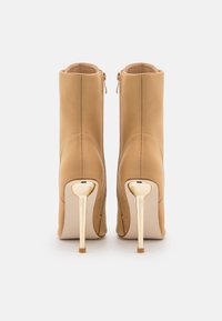 Bottines beige en cuir lisse, dotées d'un talon haut doré et d'une fermeture éclair latérale. Texture lisse avec une silhouette épurée.