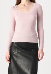 Haut à manches longues côtelé en rose pâle, avec un col rond et une coupe ajustée. Associé à une jupe en cuir noire, mettant en valeur la silhouette.